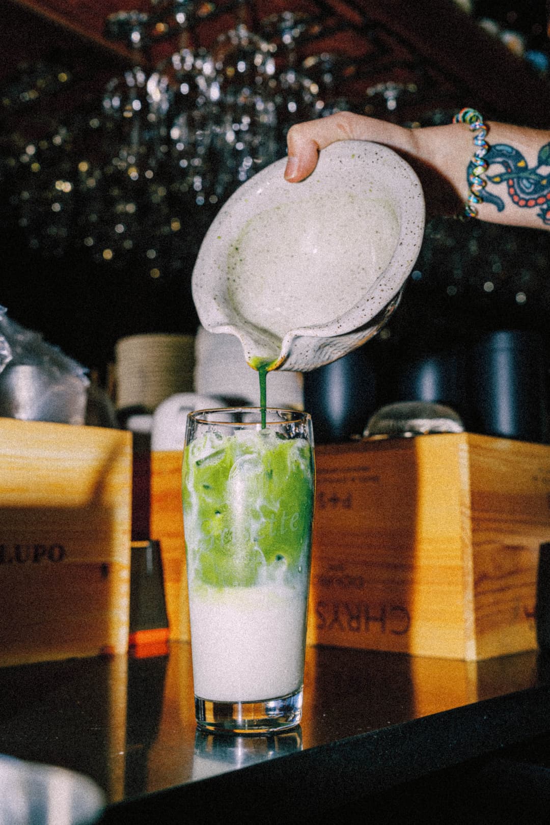 
Person pours matcha into a tall glass with ice and milk. 