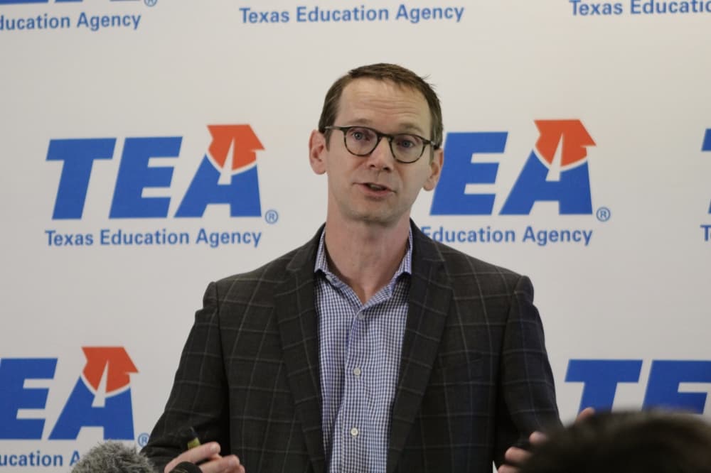 Mike Morath, in glasses and a blazer, speaks in front of a Texas Education Agency backdrop.