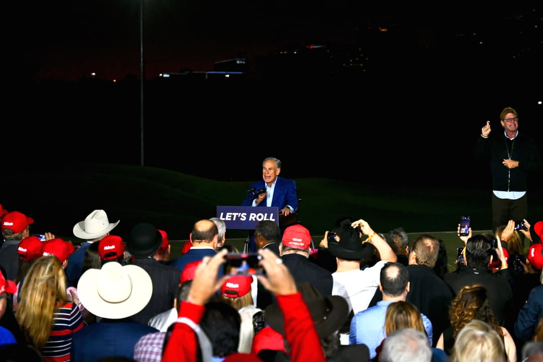 Gov. Greg Abbott speaks at podium reading "Let's Roll" before a crowd in red caps at a Nov. 9 rally.