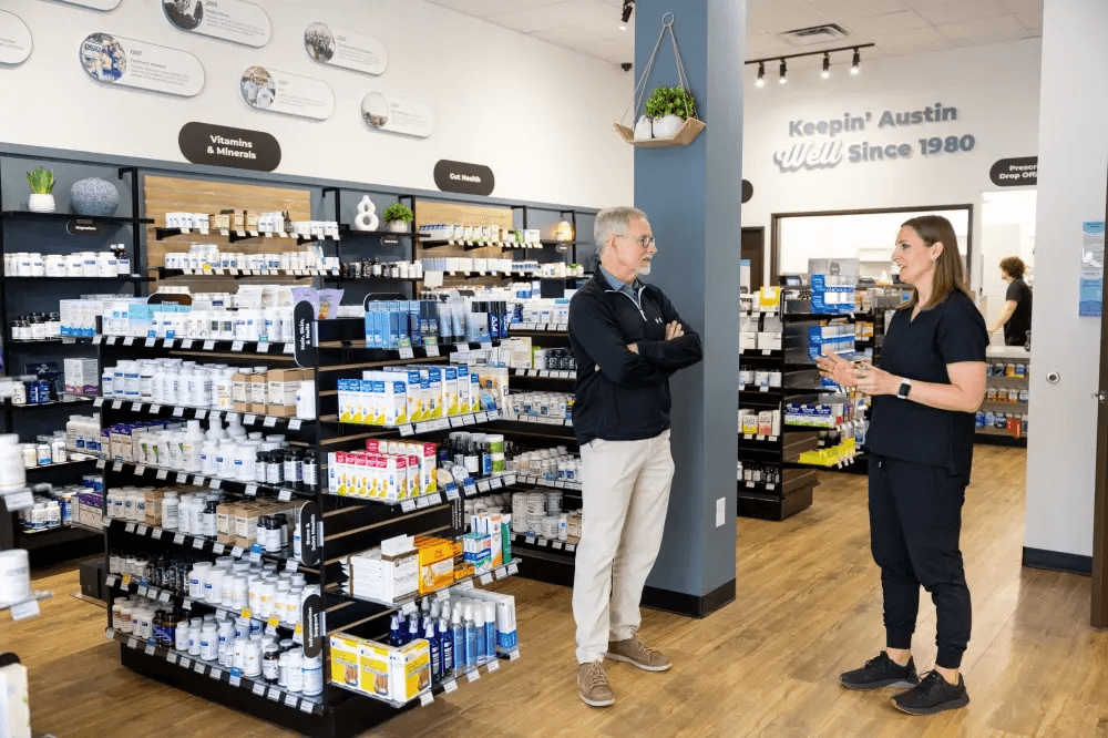 A man and a woman talk inside of Peoples Pharmacy with shelves of product behind them.