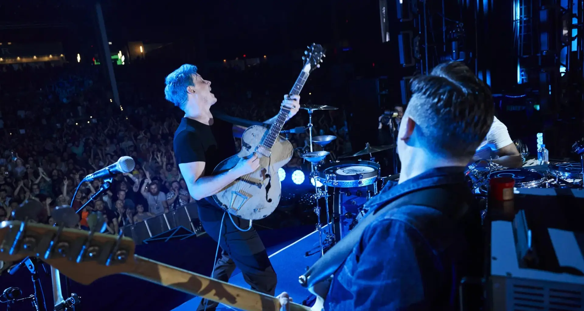 jack white performs on stage with blue hair and wearing all black front of a large crowd while holding a white guitar