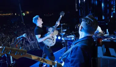 jack white performs on stage with blue hair and wearing all black front of a large crowd while holding a white guitar