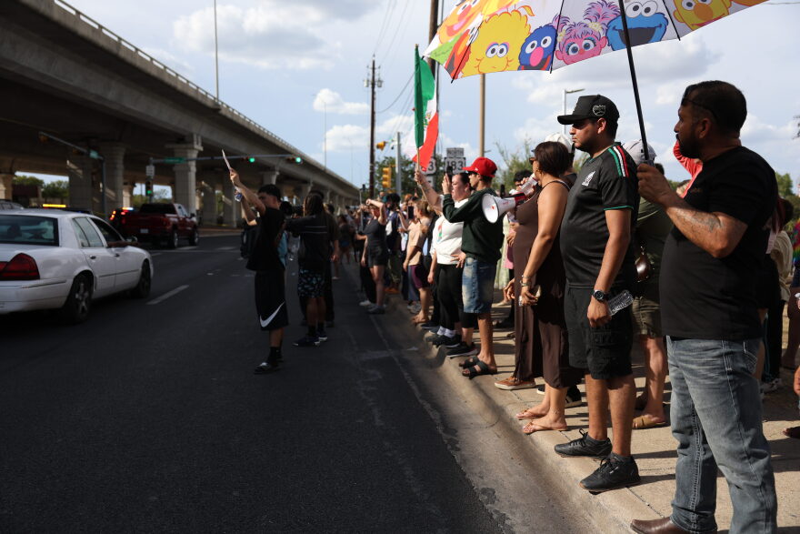 Protesters line a sidewalk along a busy street.