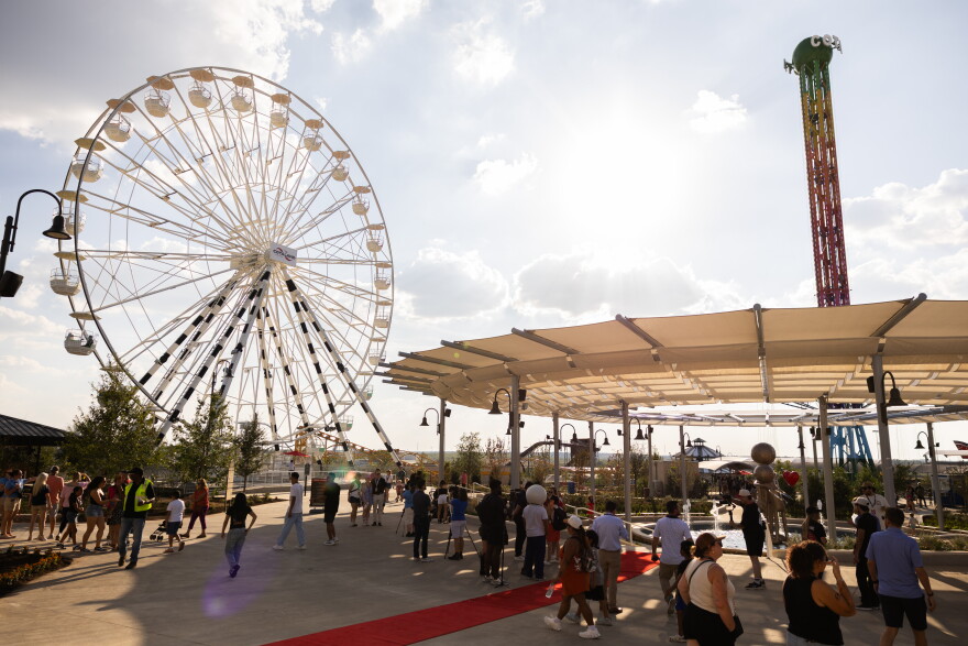 The entrance of the COTALAND theme park on a sunny day, featuring a Ferris wheel and a moderate crowd.