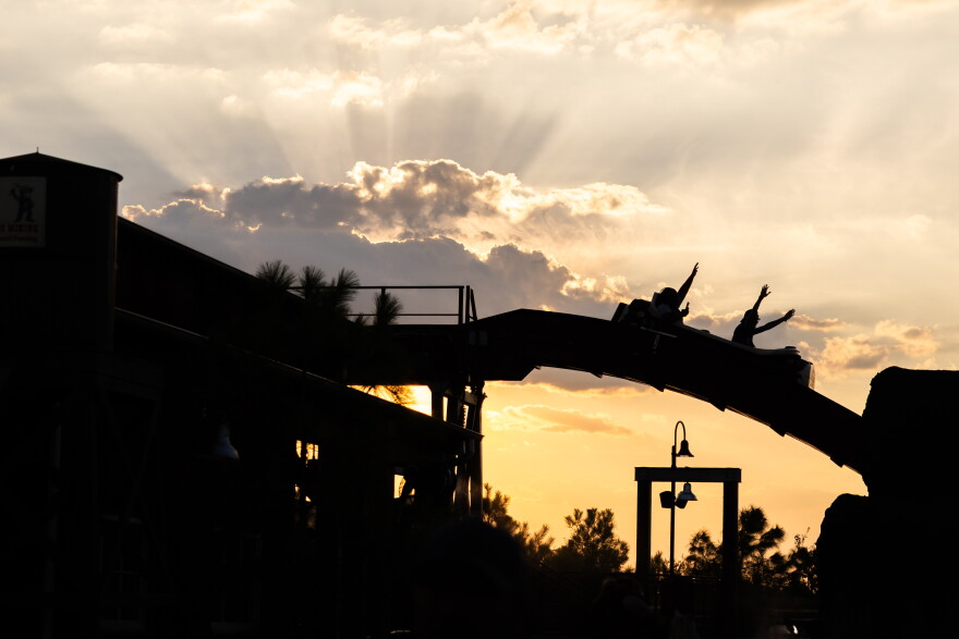 Two people raise their hands up while riding a log flume ride during sunset.