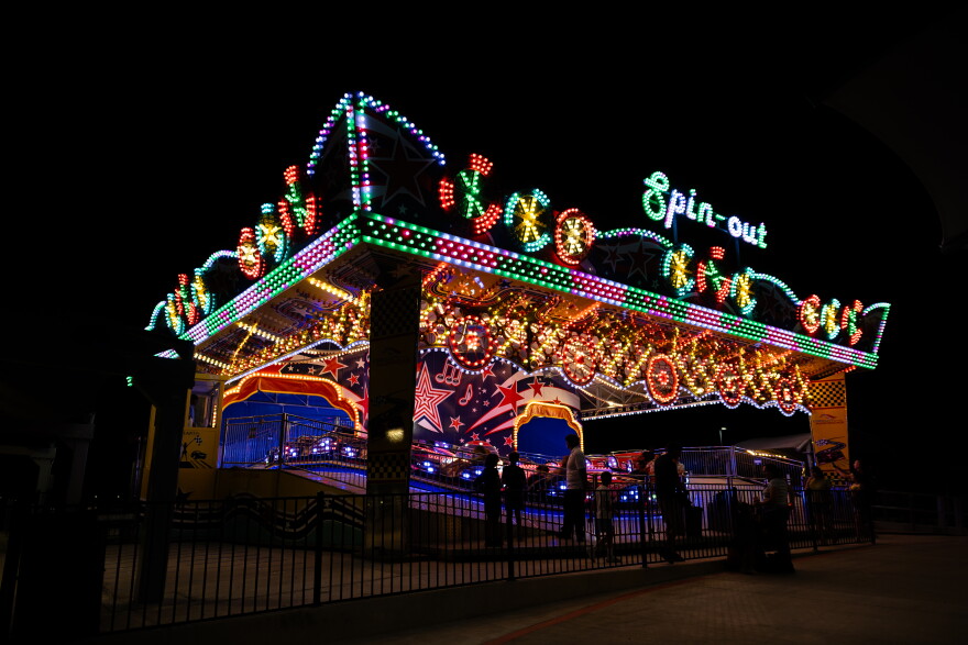 A colorfully lit spinning ride stands out against a black sky. 
