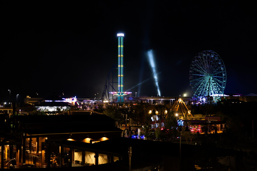Several parts of COTALAND are lit up against the night sky, including a tower ride and the Ferris wheel.