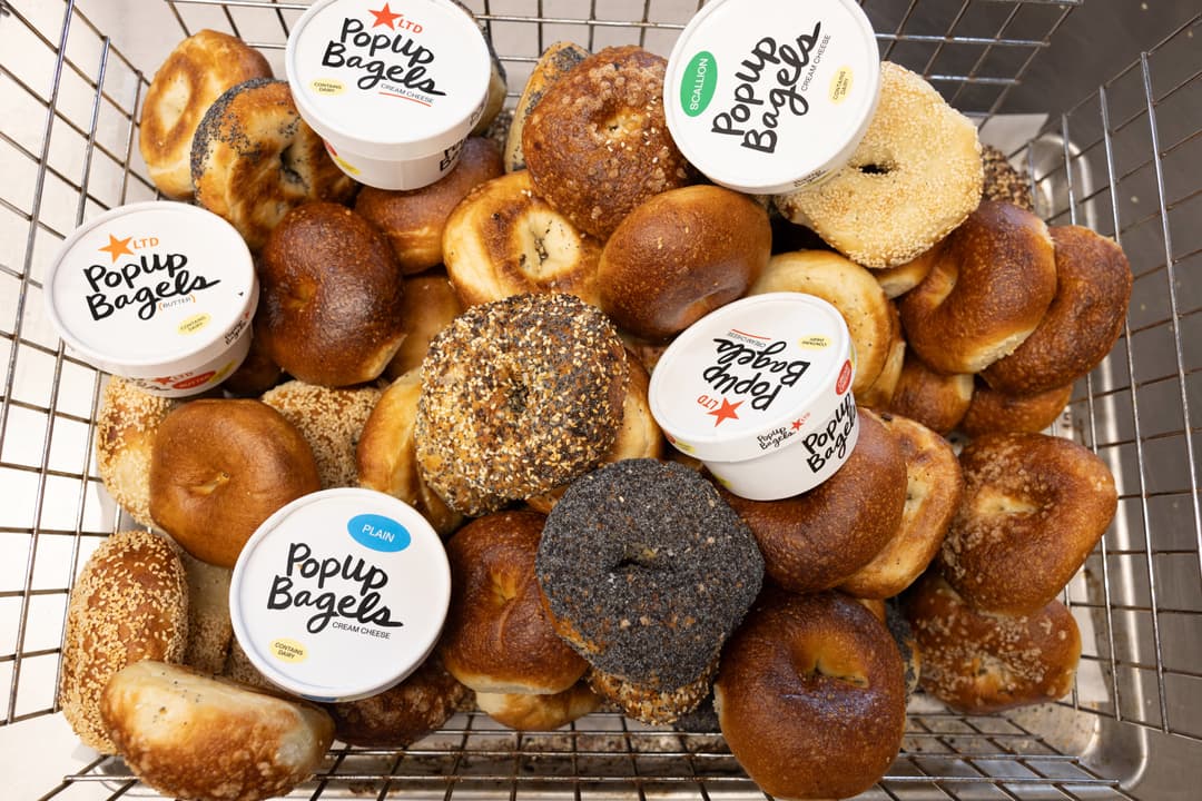 Wire basket filled with assorted bagels and tubs of PopUp Bagels cream cheese and butter spreads.