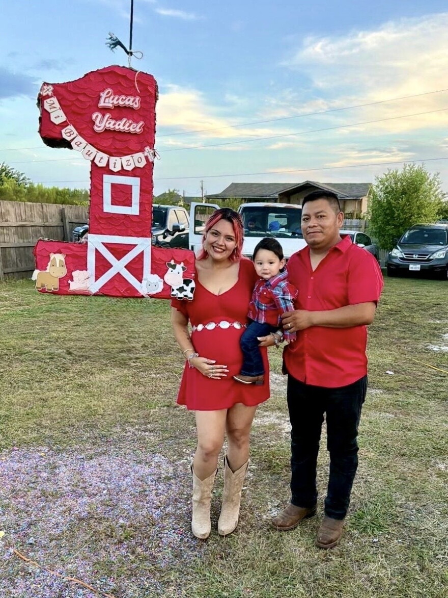 A pregnant woman and a man holding a baby. A piñata of a number one hangs besides them.
