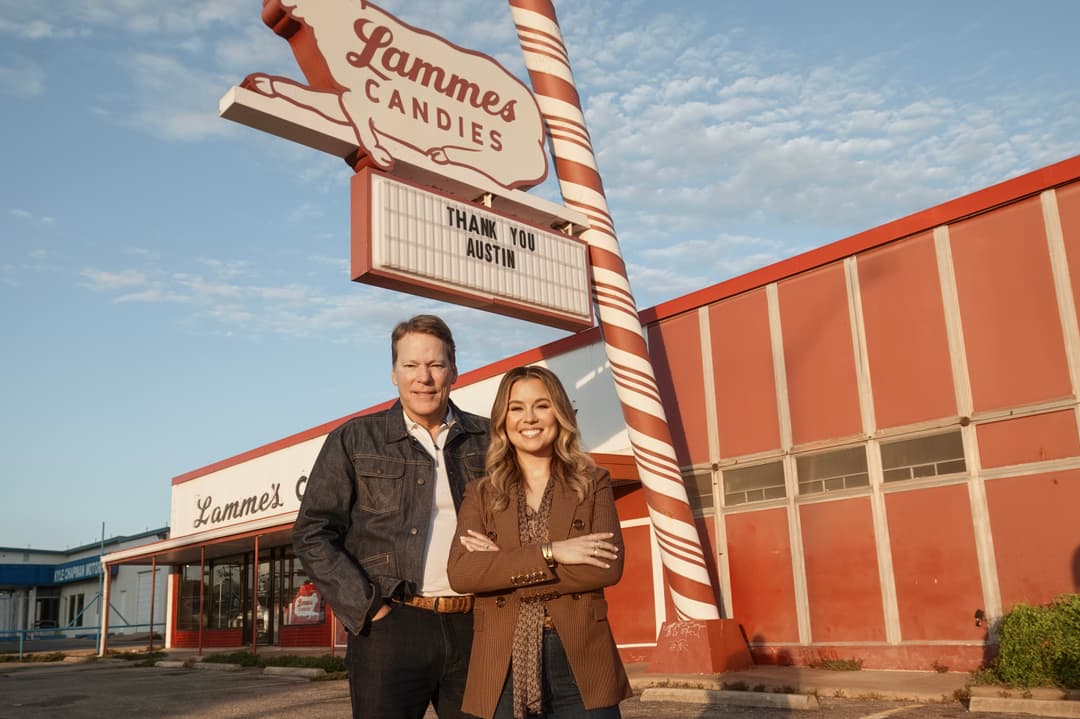A man and a woman stand in the parking lot of the former Lammes Candies store on Airport Boulevard. Behind them are the giant candy cane pole and lamb sign, with a marquee reading "Thank you Austin."