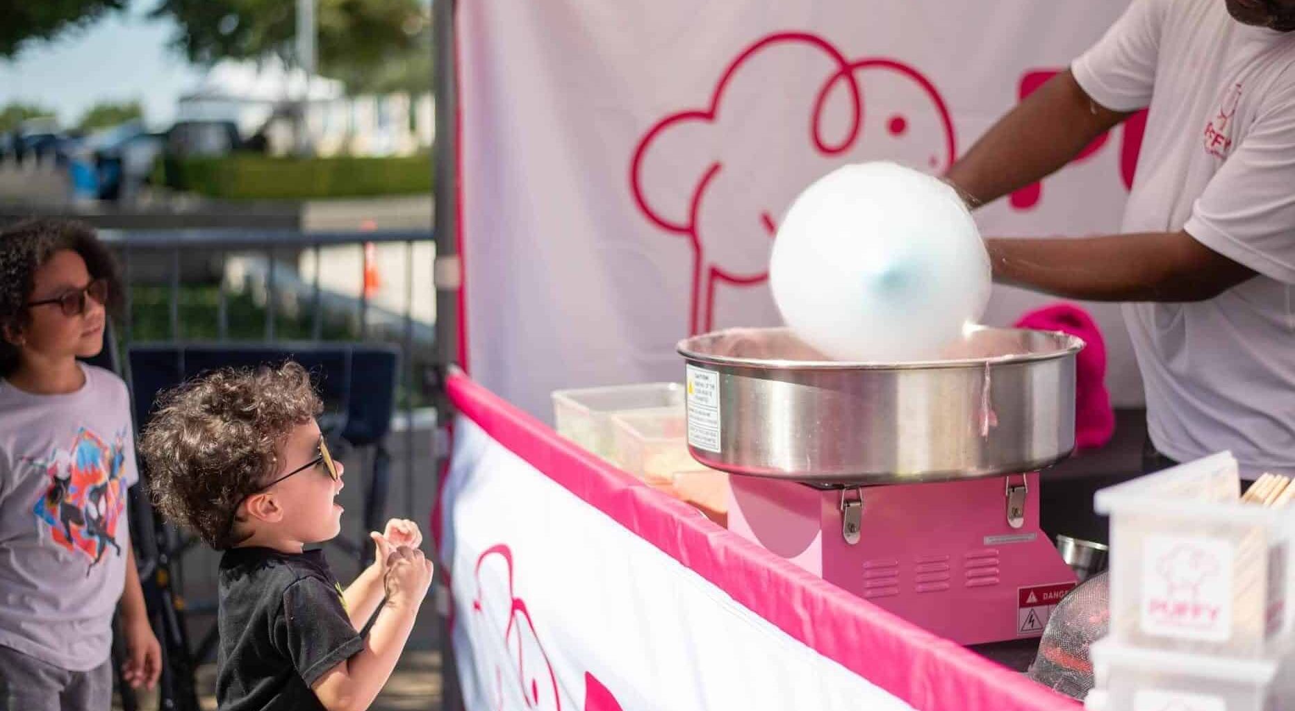 Children at fair getting cotton candy from vendor booth.
