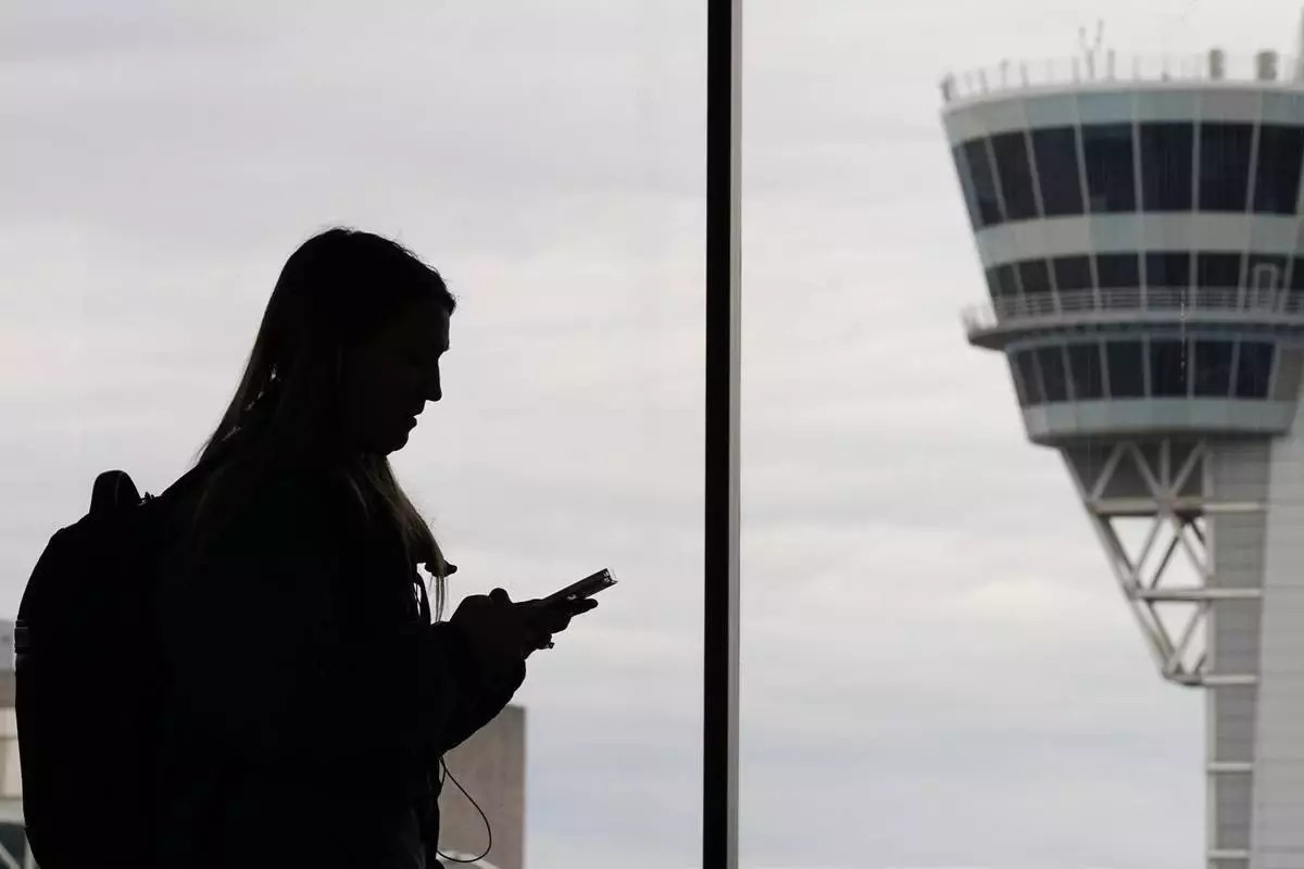 FILE - A traveler with a smartphone walks past an air traffic control tower at Philadelphia International Airport in Philadelphia on March 27, 2026. (AP Photo/Matt Rourke, File)