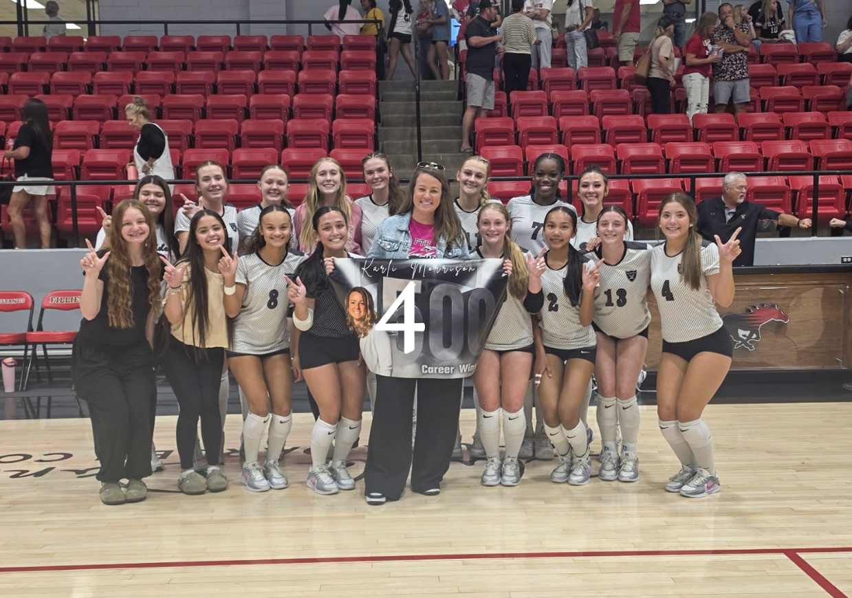 Girls' volleyball team posing for a milestone photo with a banner that reads '400 Career Wins' in a gym with red bleachers behind them.