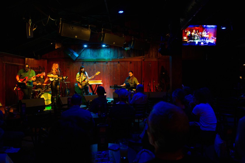 Four musicians play on a stage in front of a crowd of people illuminated by blue stage light.