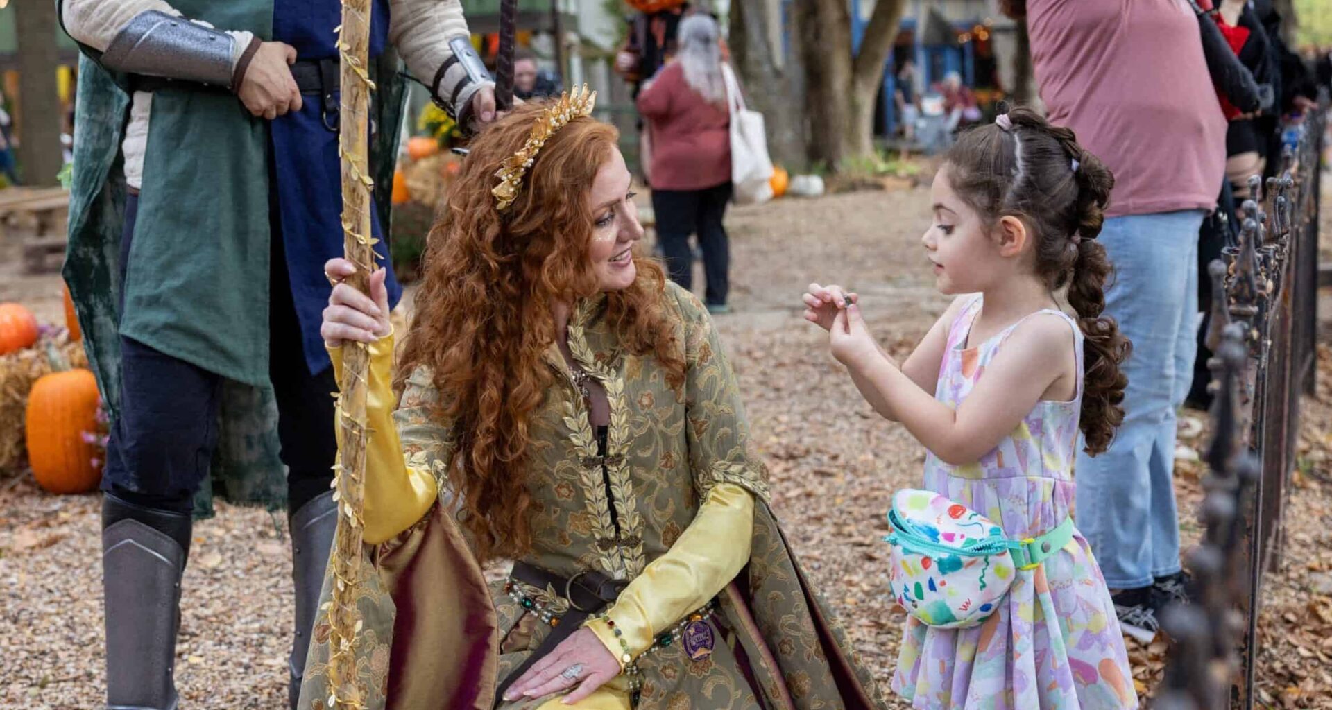 Young girl meets a woman dressed as a fairy tale princess at fall festival.