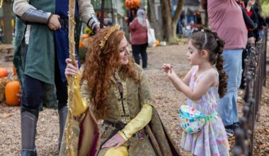 Young girl meets a woman dressed as a fairy tale princess at fall festival.