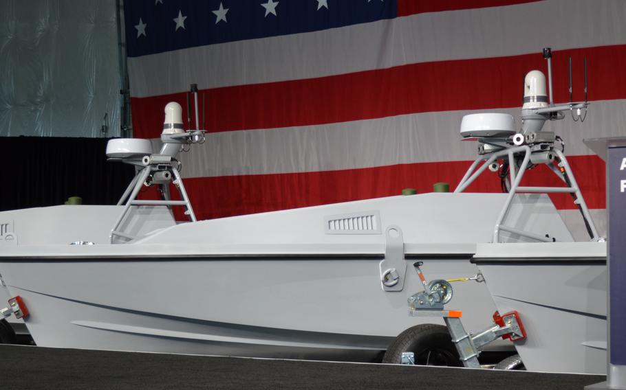 A boat-like military drone sits on display on a stage in front of a large U.S. flag.