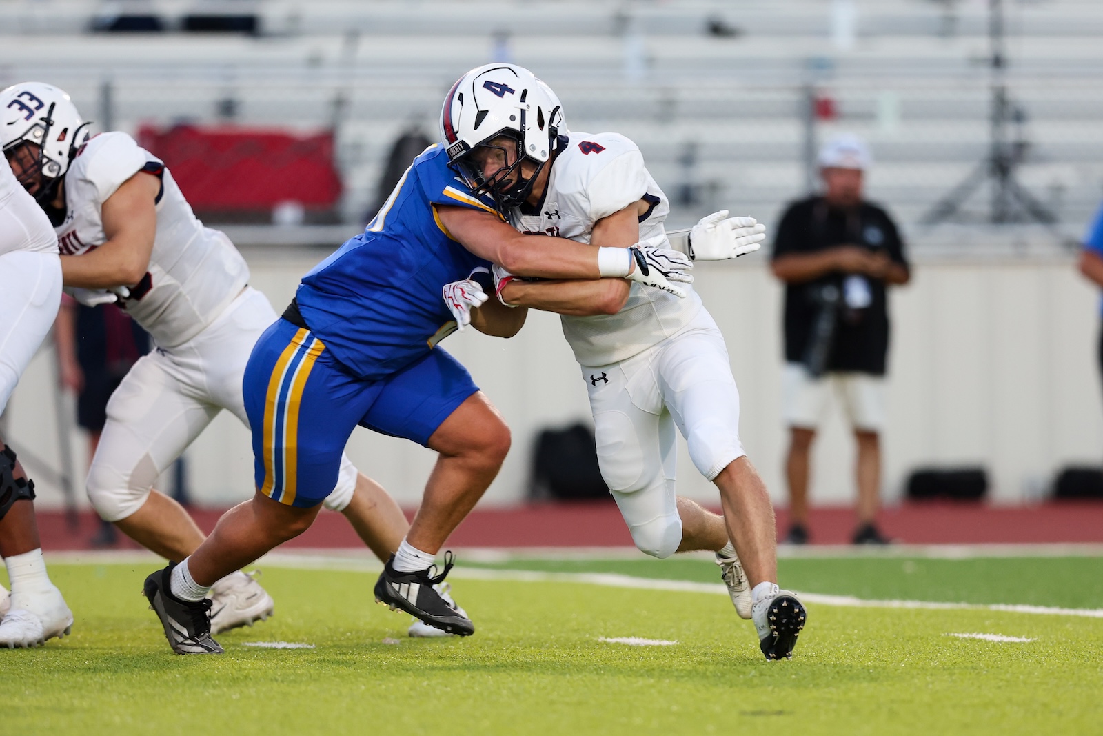 Seabolt Chase-17816 | Press Pass Sports Two football players collide in a tackle: a white‑jersey player grips a blue‑jersey opponent on a green field.