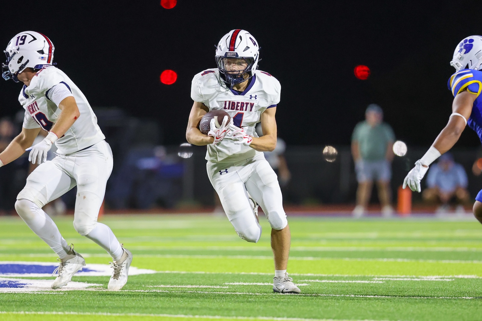 Seabolt Chase-18224 | Press Pass Sports Soccer? No—American football: a Liberty player carries the ball while running downfield at night on a green turf field.
