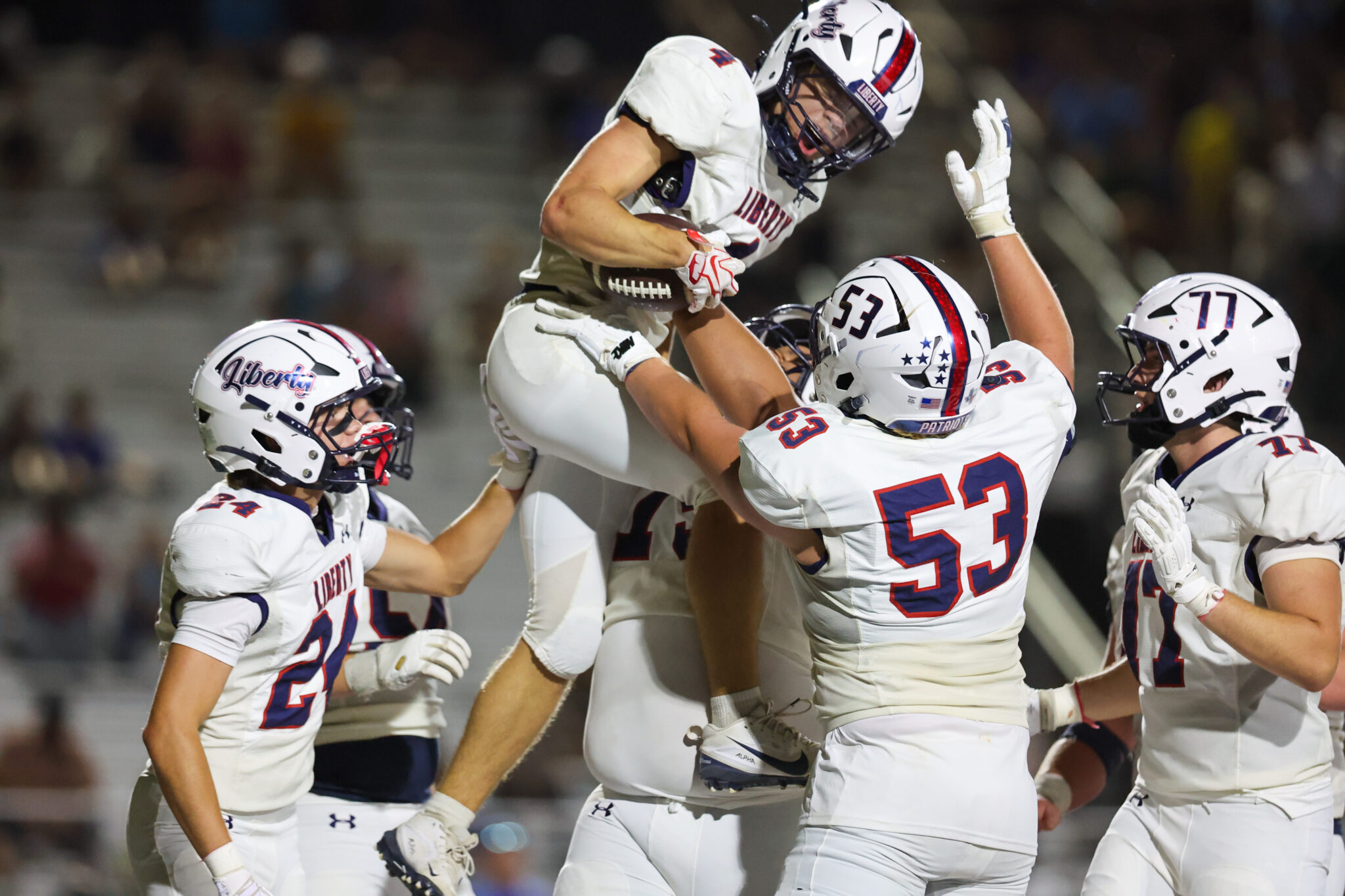 Liberty University football players in white uniforms celebrate a teammate being lifted in the air on the field.
