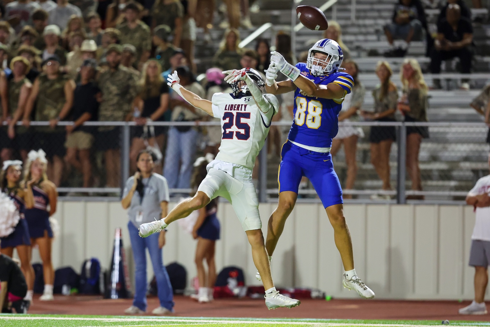Seabolt Chase-18716 | Press Pass Sports Two football players leap to intercept the ball, one in white Liberty jersey (#25) and the other in blue (#88, in mid-air).