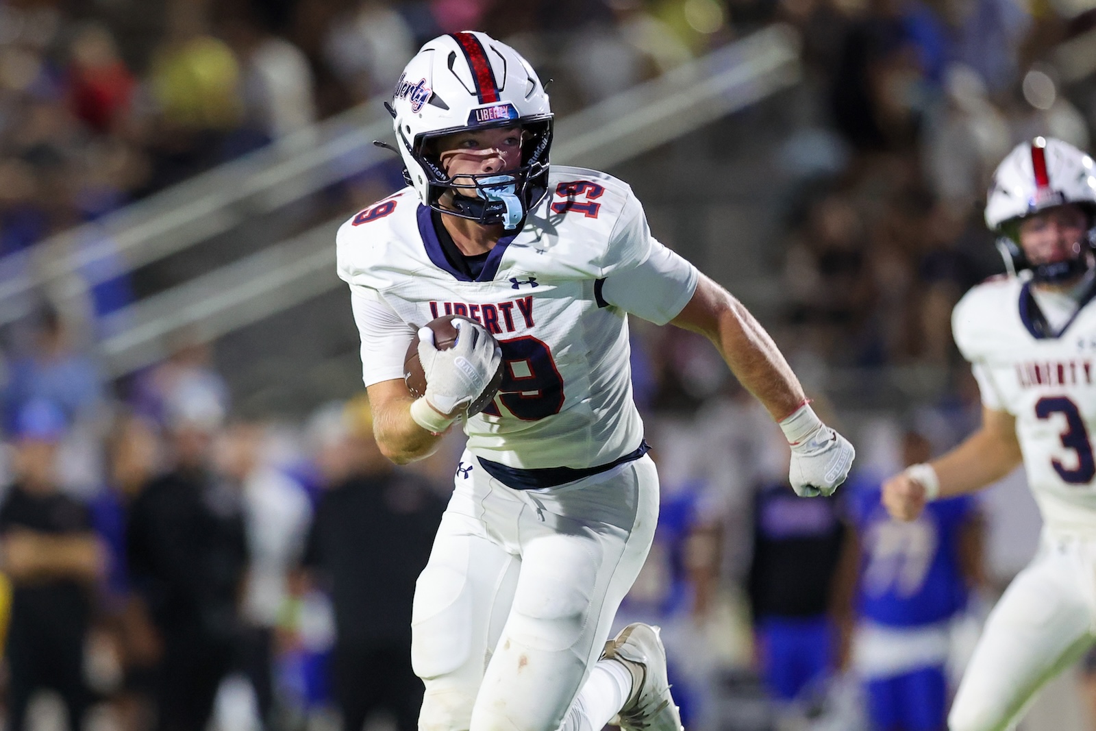 Seabolt Chase-18868 | Press Pass Sports Liberty University football player in white jersey #9 runs with the ball on a field, crowd in the stands behind him.