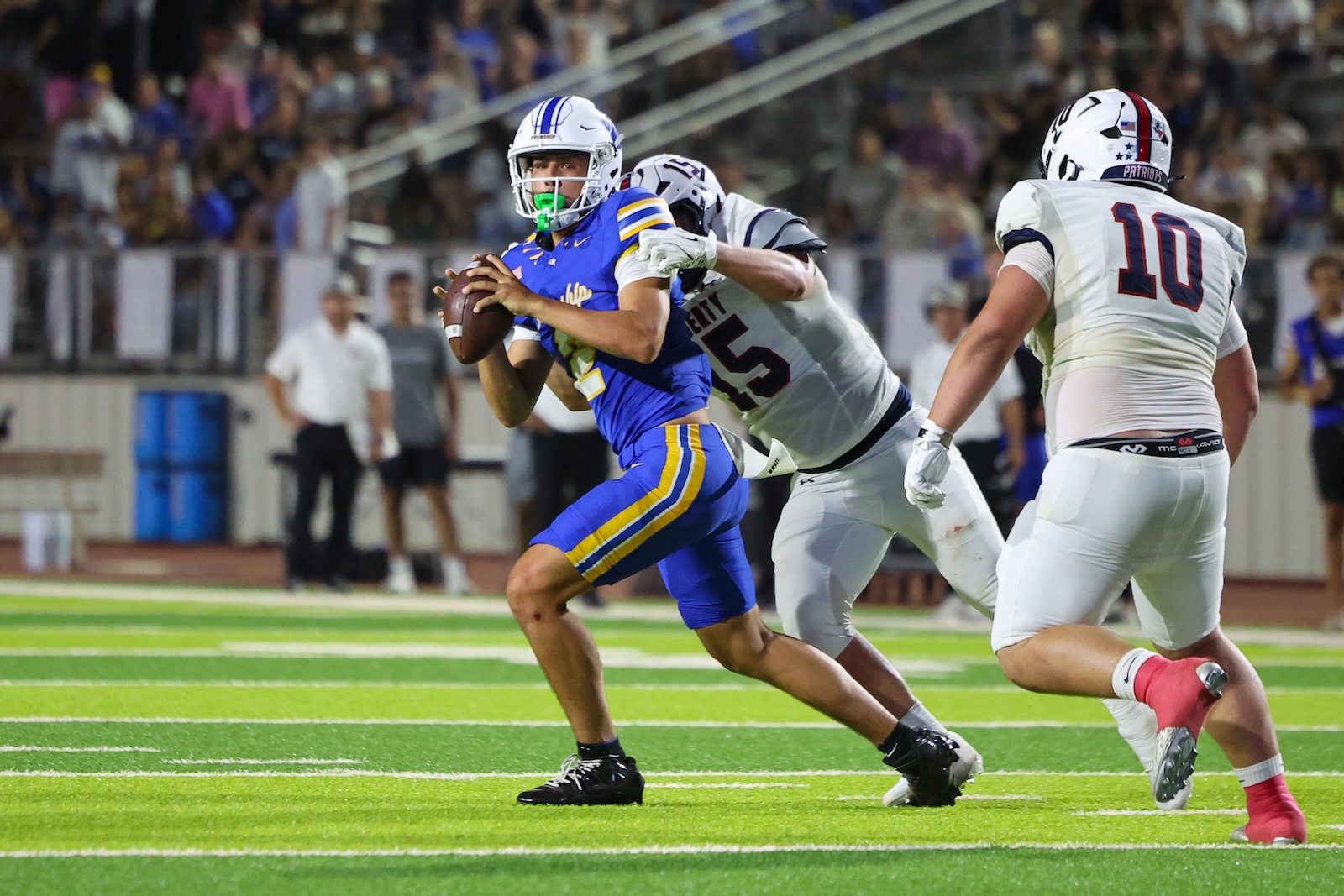 Seabolt Chase-25567 | Press Pass Sports Football player in blue and yellow carries the ball as a white-uniform defender grabs at him on a bright green field with a crowded stands background.