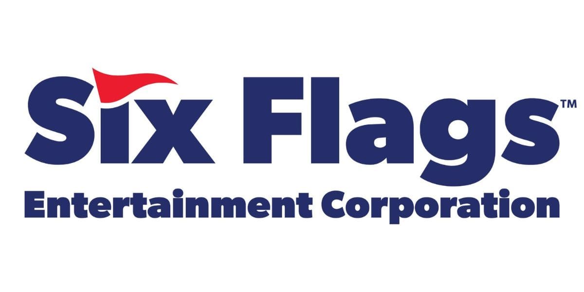 The image shows the logo of Six Flags Entertainment Corporation with the company name in bold blue letters. A small red flag icon tucks within the "x" of "Six." The words "Entertainment Corporation" are written below in a smaller blue font, reflecting the branding after recent discussions about a potential Six Flags merger, in big theme park news. Six Flags park presidents
