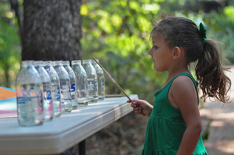 A little girl outdoors playing with plastic bottles filled with water