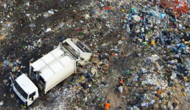 A garbage truck is on a waste pile, with workers collecting debris in a landfill area.