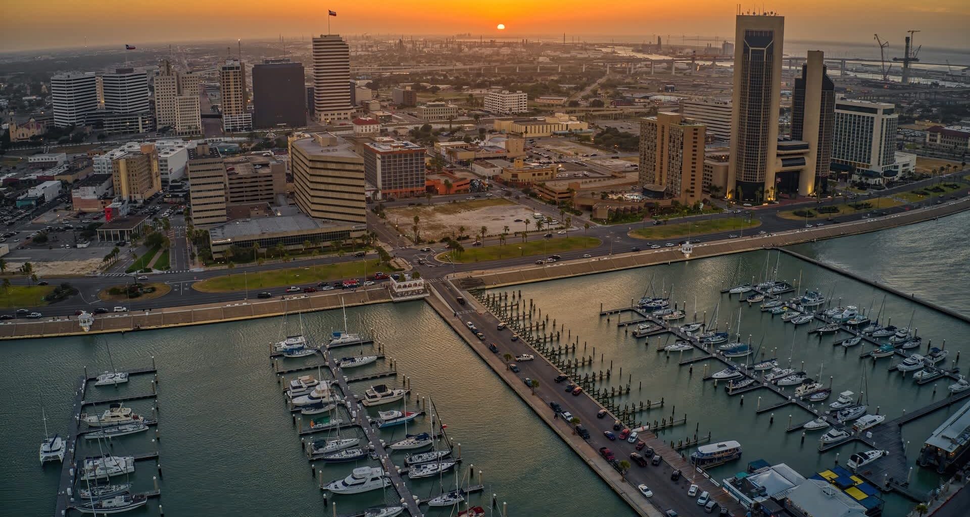 A waterfront view of Corpus Christi, Texas, marina with boats and a skyline at sunset.
