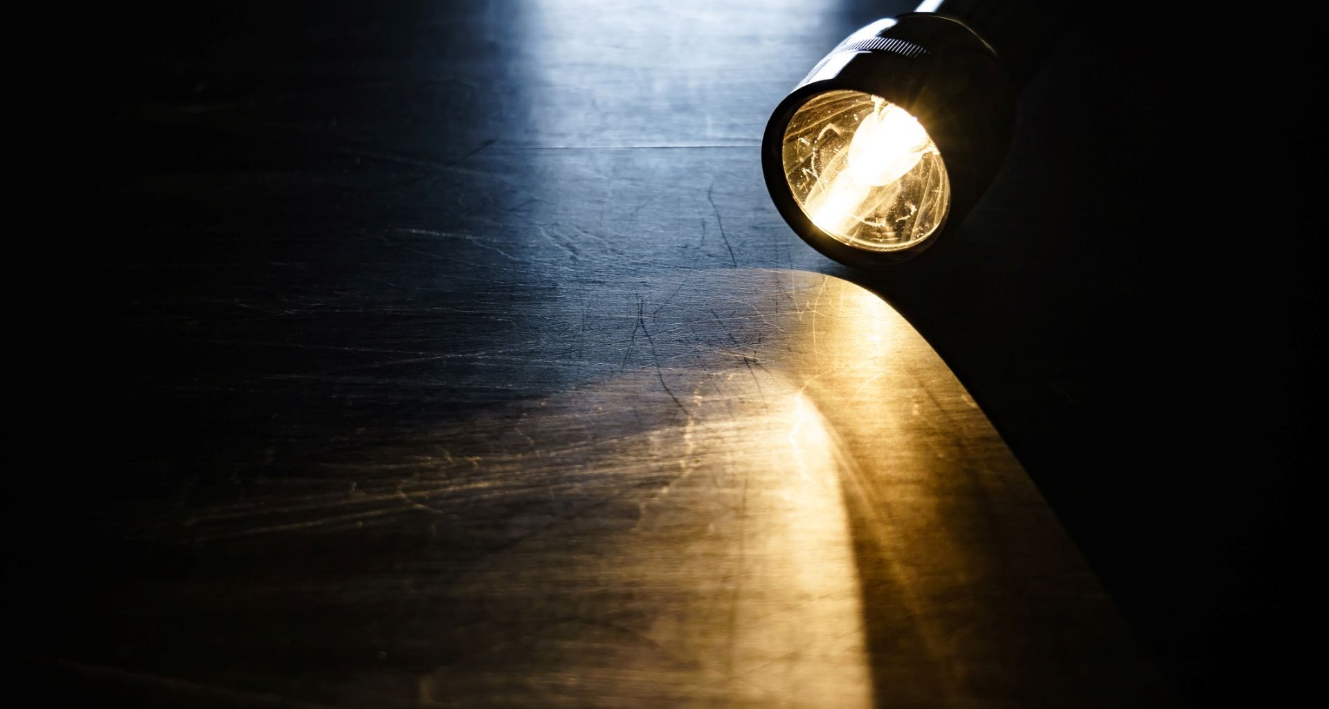 A lit flashlight on a wooden table.