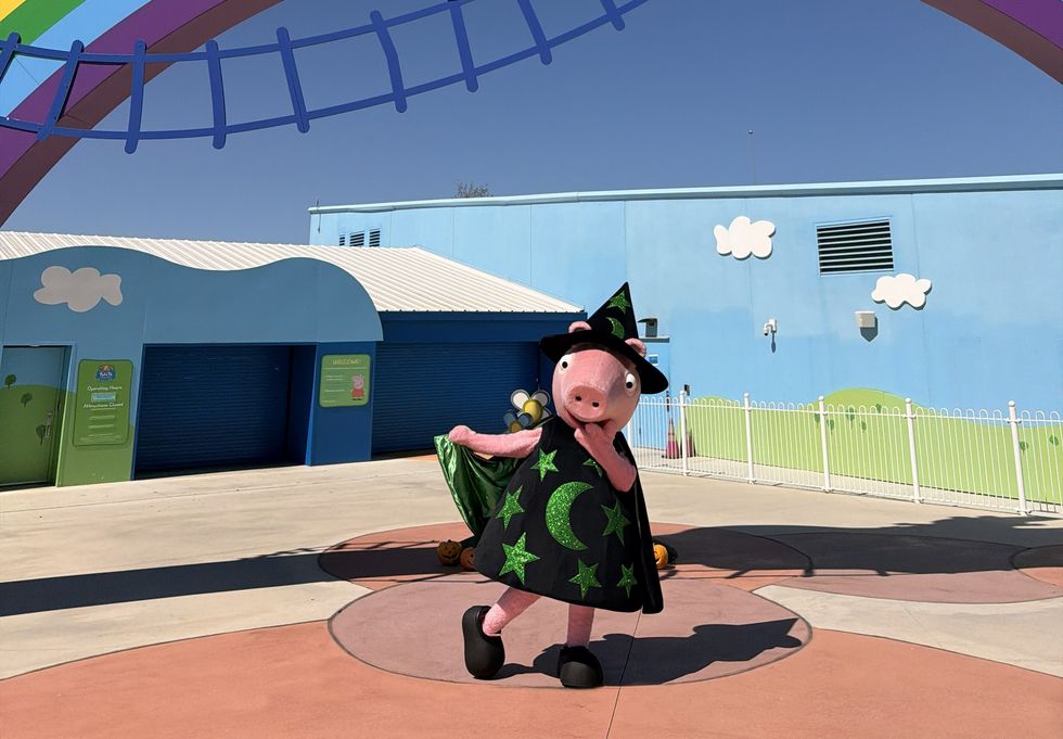Peppa Pig in wizard costume under a rainbow arch at a colorful theme park.