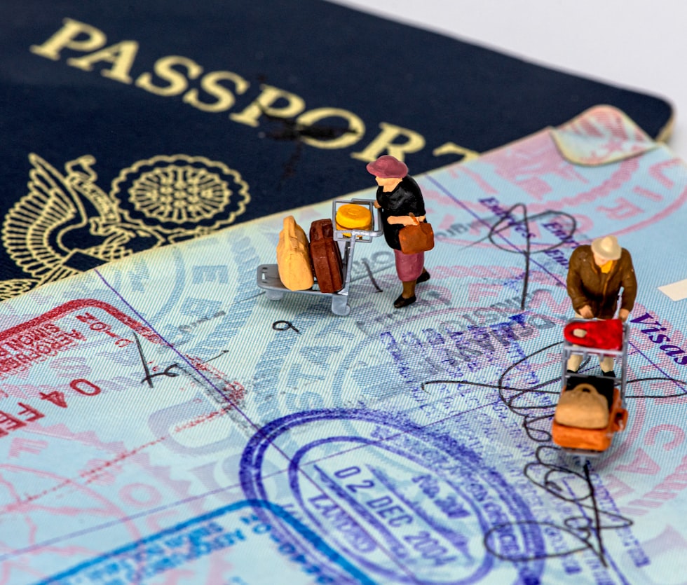 Two miniature figures with luggage carts on a passport page with travel stamps