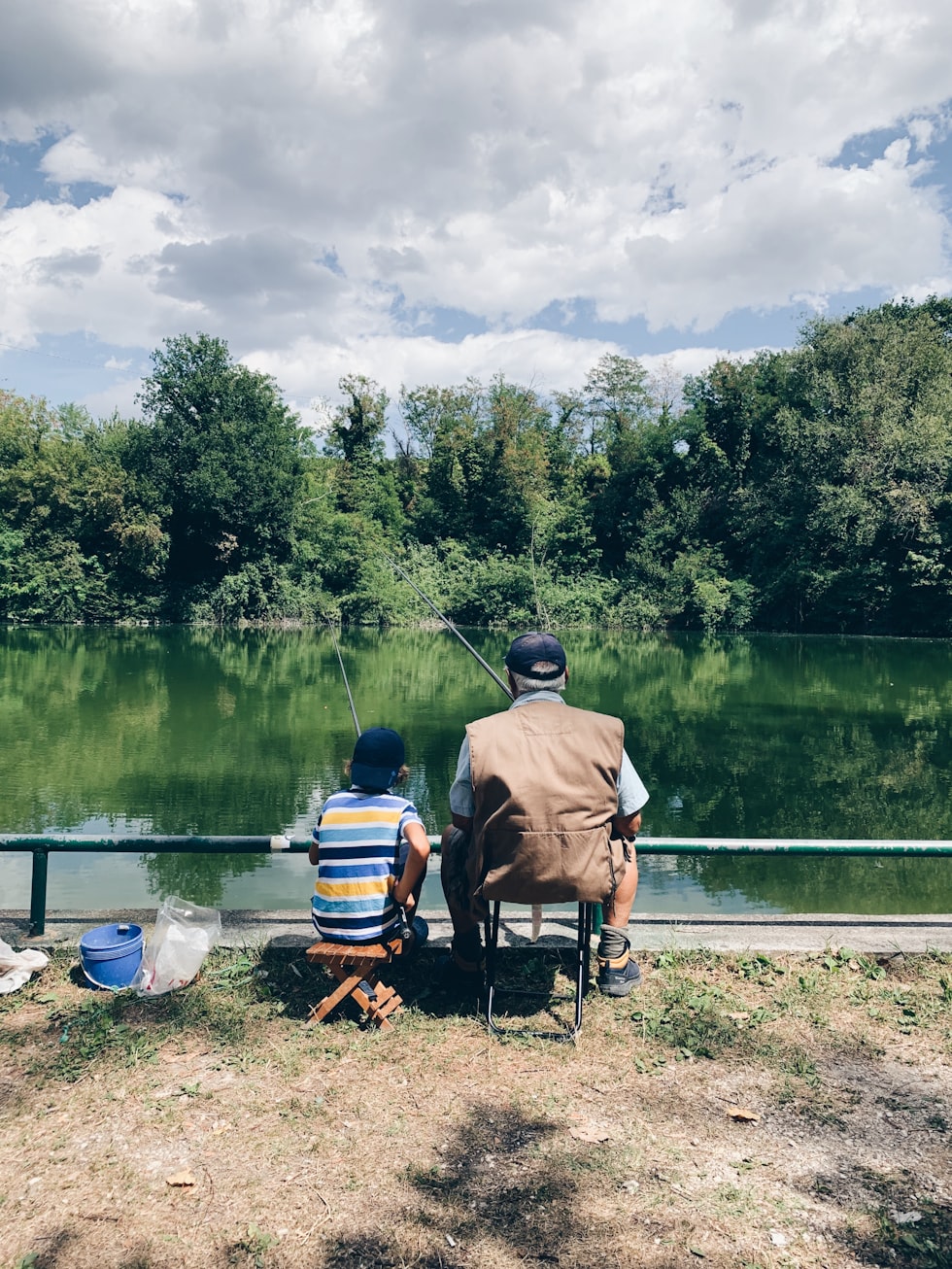 An adult and a child fishing with rods on a riverbank