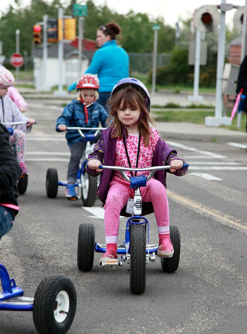 Young girl in helmet rides tricycle on a mini road