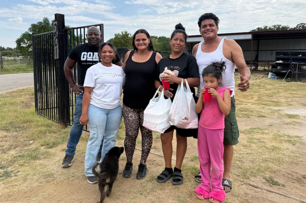 Christina Parks stands outdoors with five other people, including a child, as several hold bags of food. A small dog stands in front of the group.