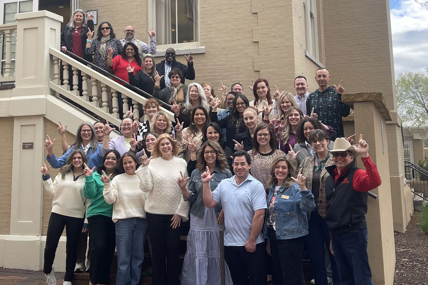 A large group poses on the steps outside the Geosciences building while making the Guns Up hand sign.