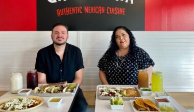 The image shows an a table with Mexican street-style tacos, queso birria tacos, onions, limes and salsas.