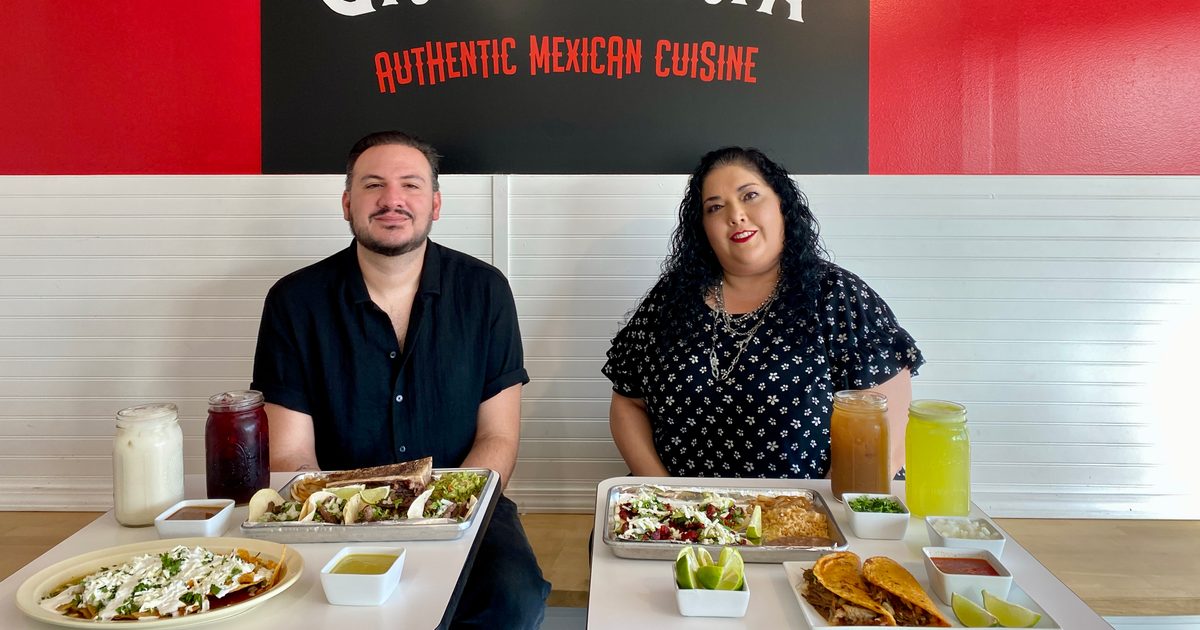 The image shows an a table with Mexican street-style tacos, queso birria tacos, onions, limes and salsas.