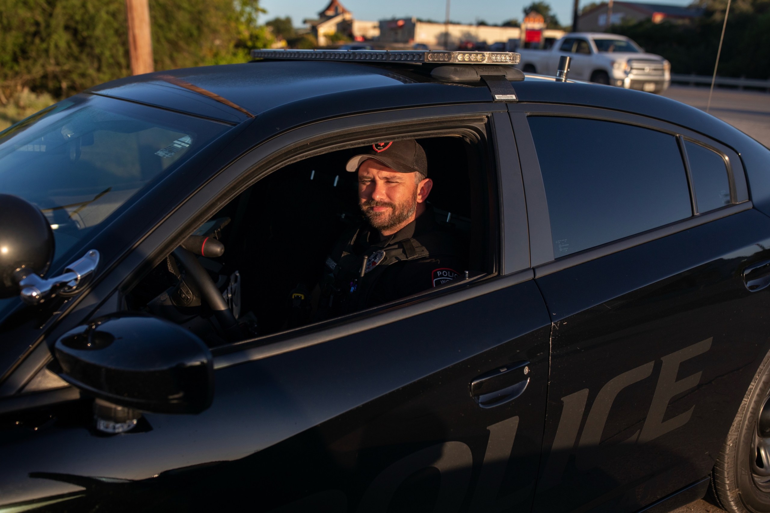 A bearded man wearing a baseball cap and a dark uniform sits in a black Charger.