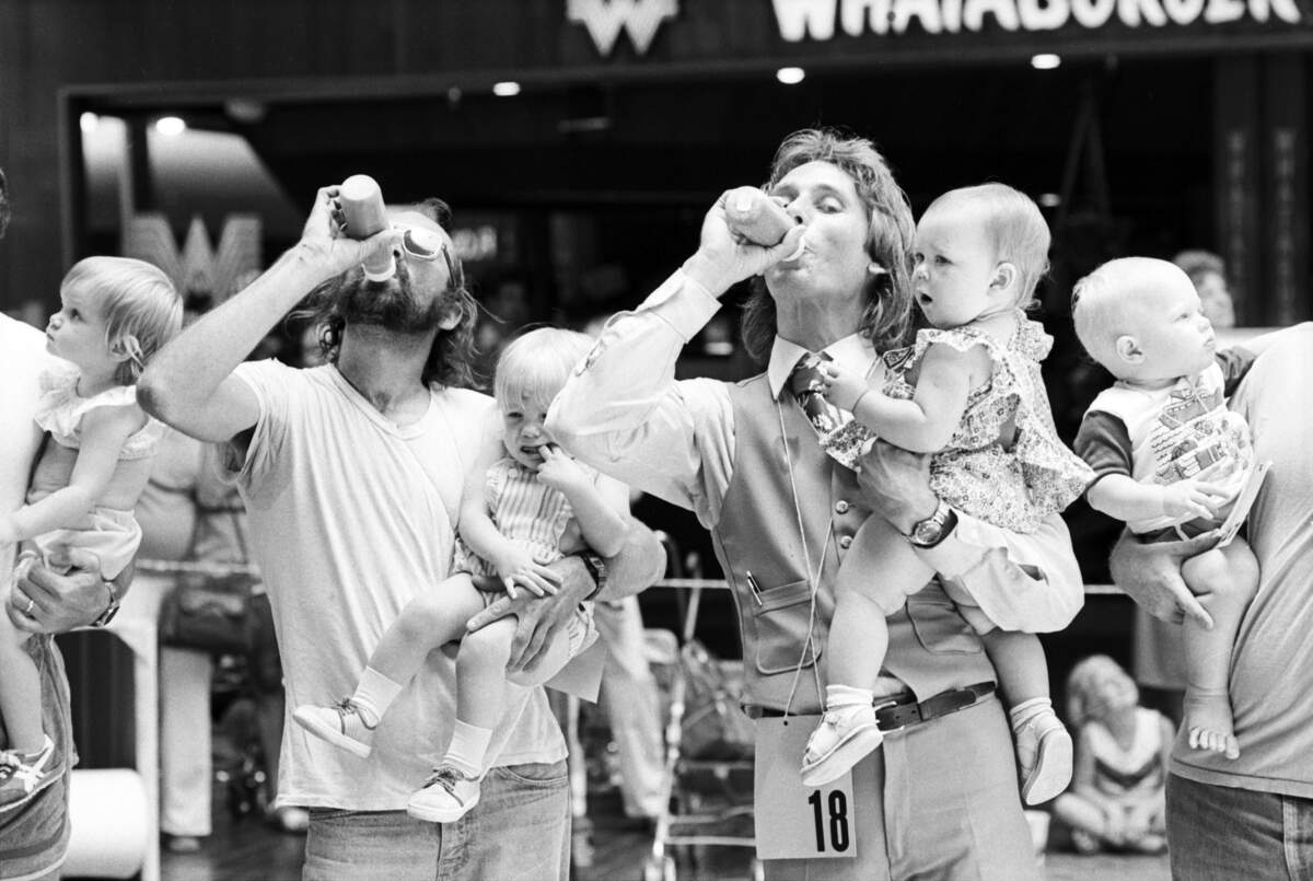 A group of fathers and their children competing in the March of Dimes "Father-Baby Olympics" at Ridgmar Mall in Fort Worth. The fathers can be seen downing the contents of a baby bottle during a competition. Kenneth Blount and his daughter Karyn Blount, 15 months old, are seen at left. [FWST photographer Rodger Mallison]