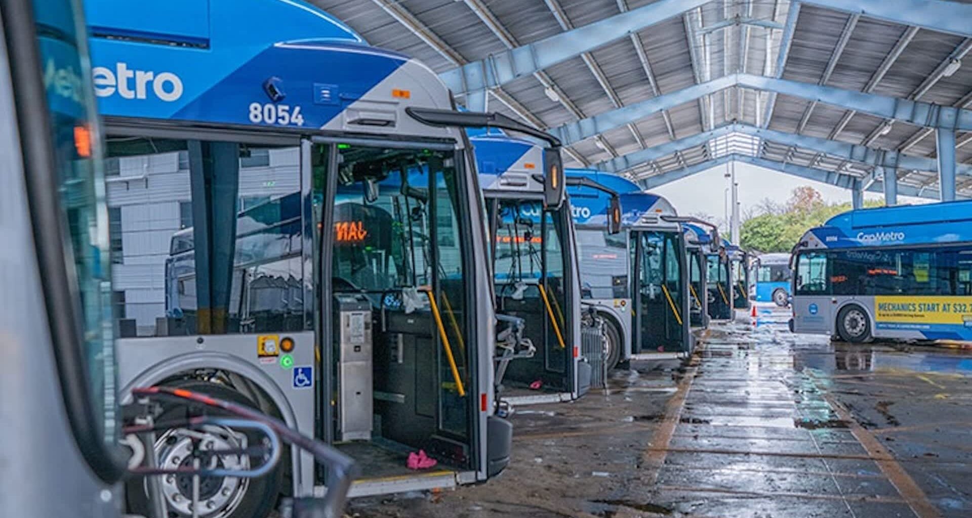 Buses parked in an indoor garage with a covered roof and wet floor.