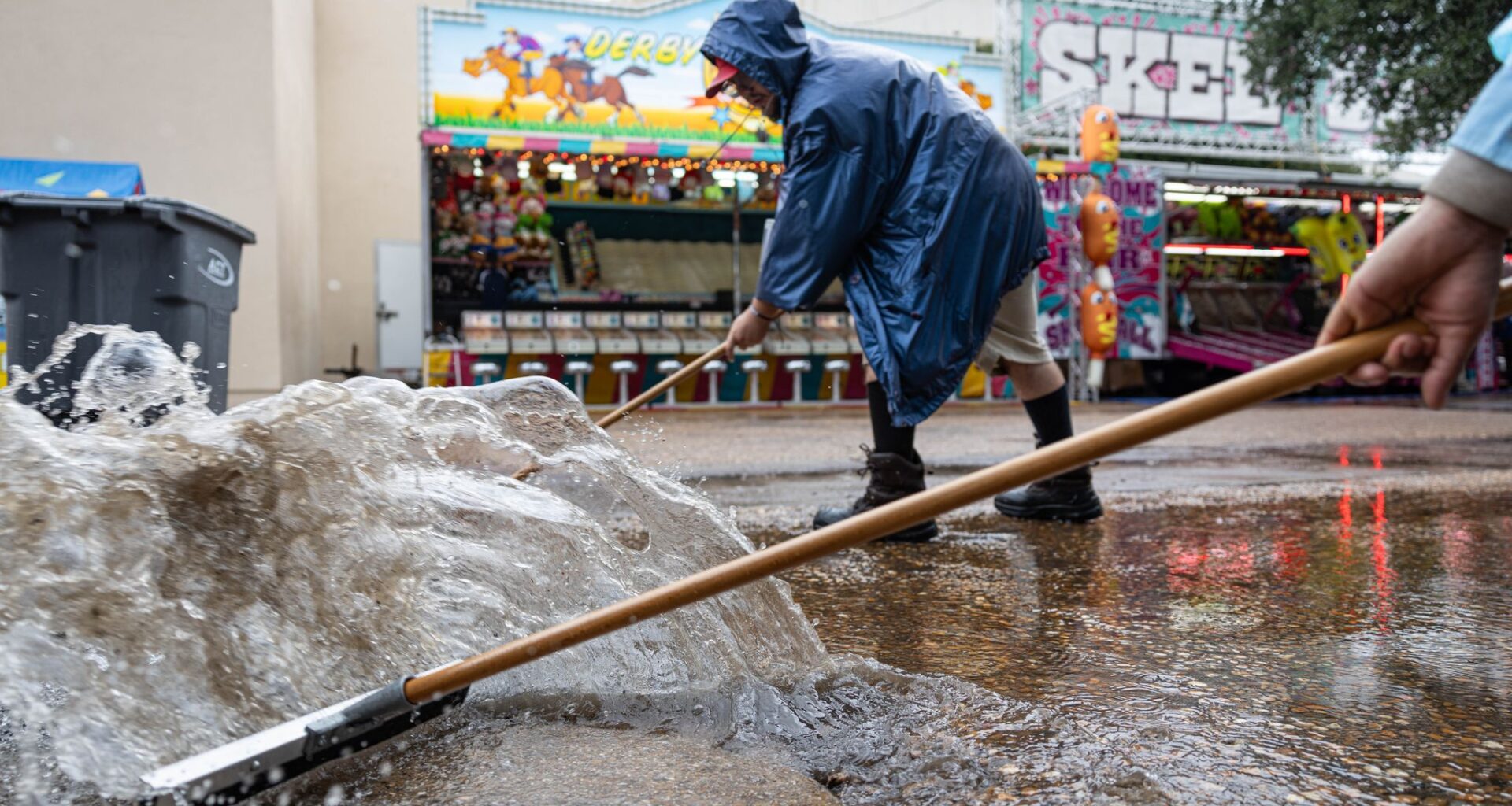 Marquist Surney and Joshua Castro, back, push water into a drain during a rainy day at the State Fair in Dallas, Thursday, Oct. 1, 2026.