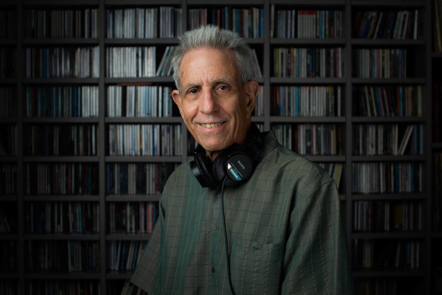 Jay Trachtenberg poses for a photo with headphones around his neck in front of a wall of CDs.