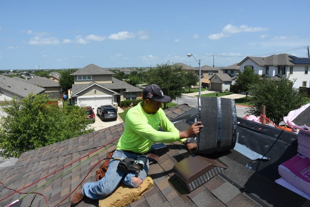 A man in a hat and neon green shirt works on a roof.