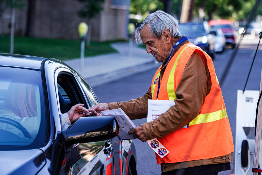 Election Judge Adam Ballinger hands a voter a sticker at a ballot drop for the Democratic primaries off location near the Denver Museum of Art, Tuesday, June 30, 2026, in Denver. (Rebecca Slezak, The Associated Press)