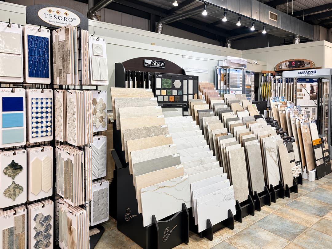 Tile and stone showroom with sample displays from Tesoro, Shaw, and Marazzi brands along rows of racks.