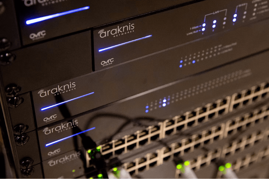 Rack of Araknis Networks switches with glowing blue LEDs and rows of Ethernet ports.