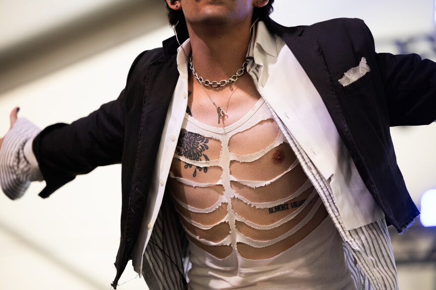 A man leans forward wearing a t-shirt with large slits in it as he performs on stage.